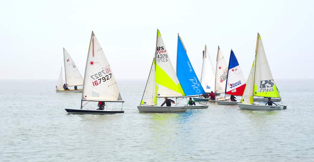 8 dinghy sailboats on the water with different coloured sails