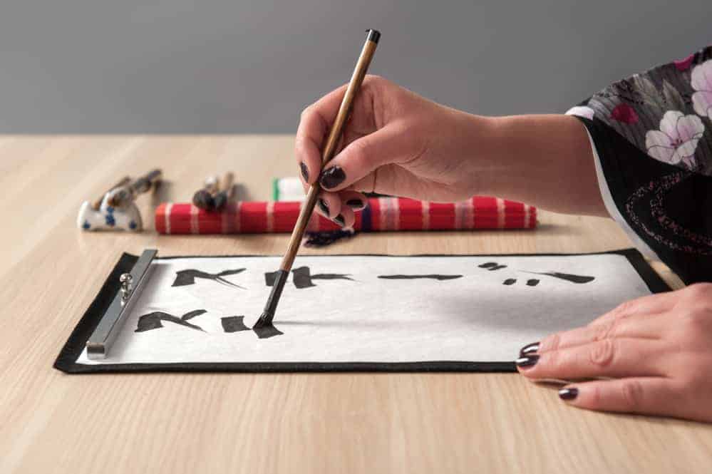 Person drawing characters in black ink as japanese calligraphy