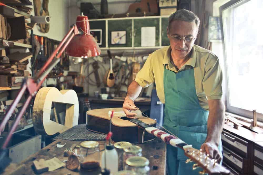 Man making a guitar in his shop wearing a shop apron in his productive hobby
