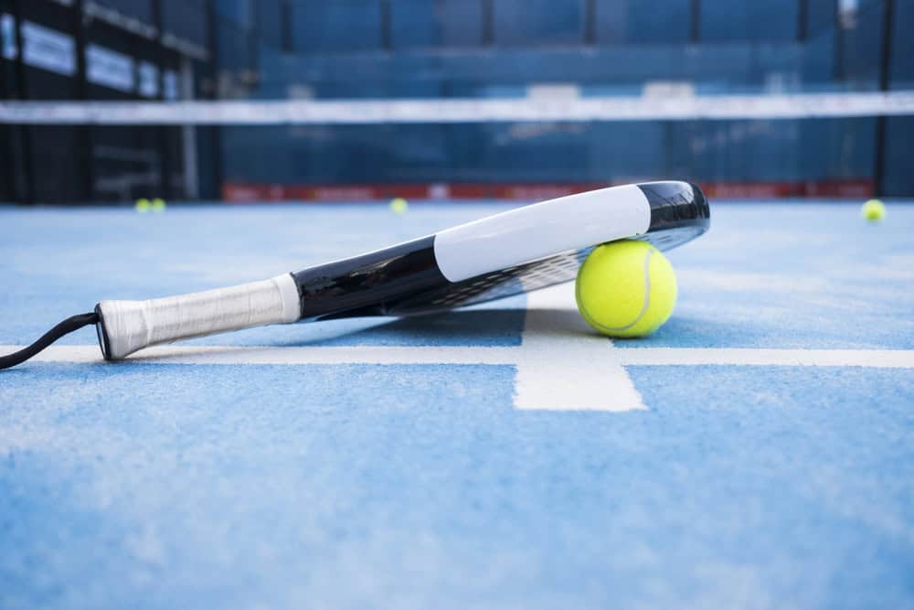 Padel racket and ball lying on a blue padel court