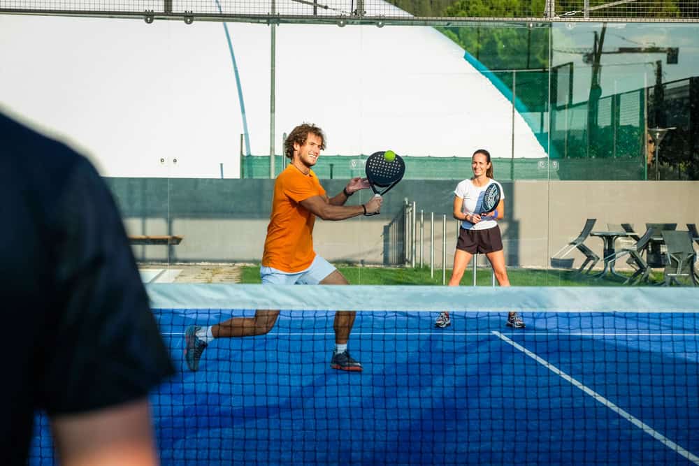 Two padel players rallying on an enclosed blue court