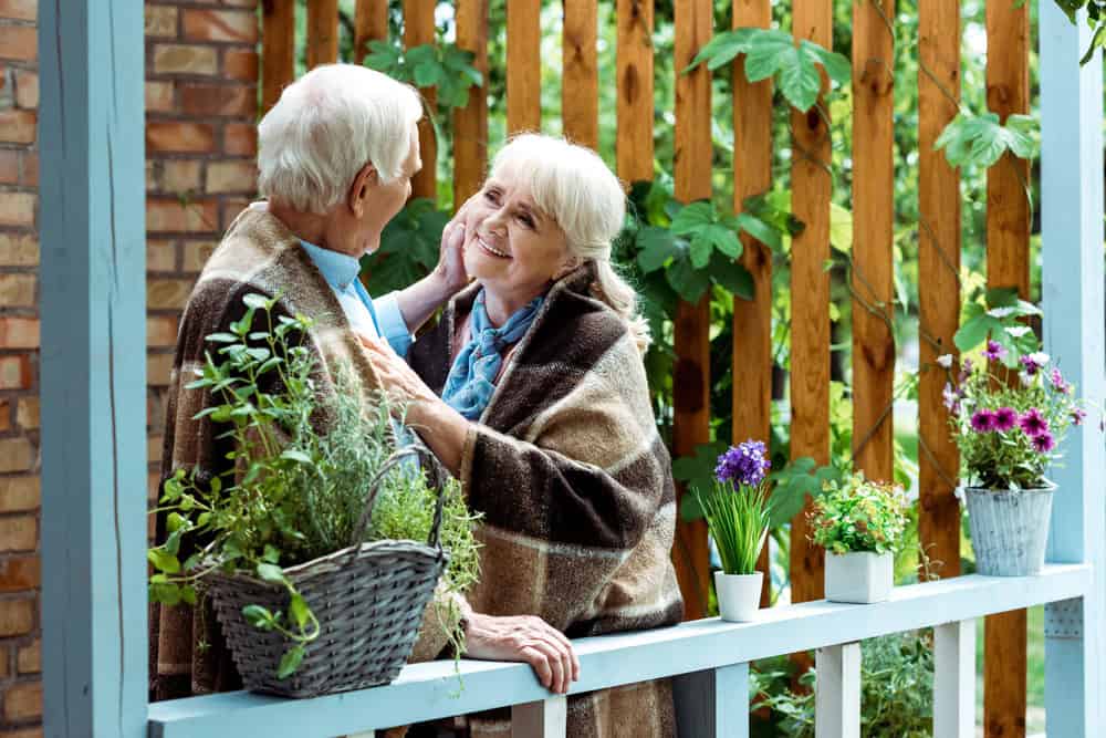 Senior couple smiling on a porch surrounded by potted plants, a retirement gardening hobby