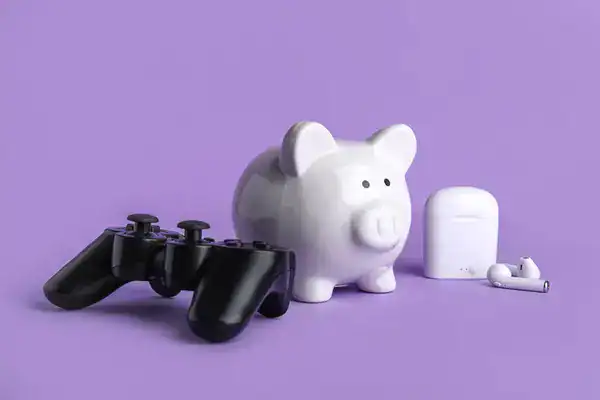 Piggy bank next to a game controller and wireless earbuds, representing the cost of hobbies